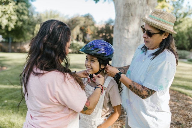 Parents helping daughter wear a helmet