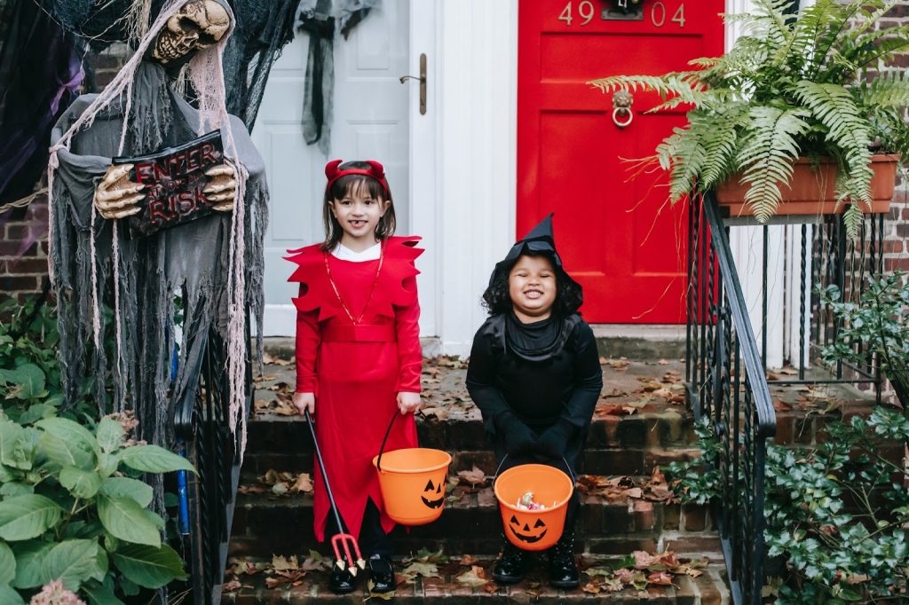 halloweenmovietriviaforkids Two girls in Halloween costumes smile with their trick or treat buckets