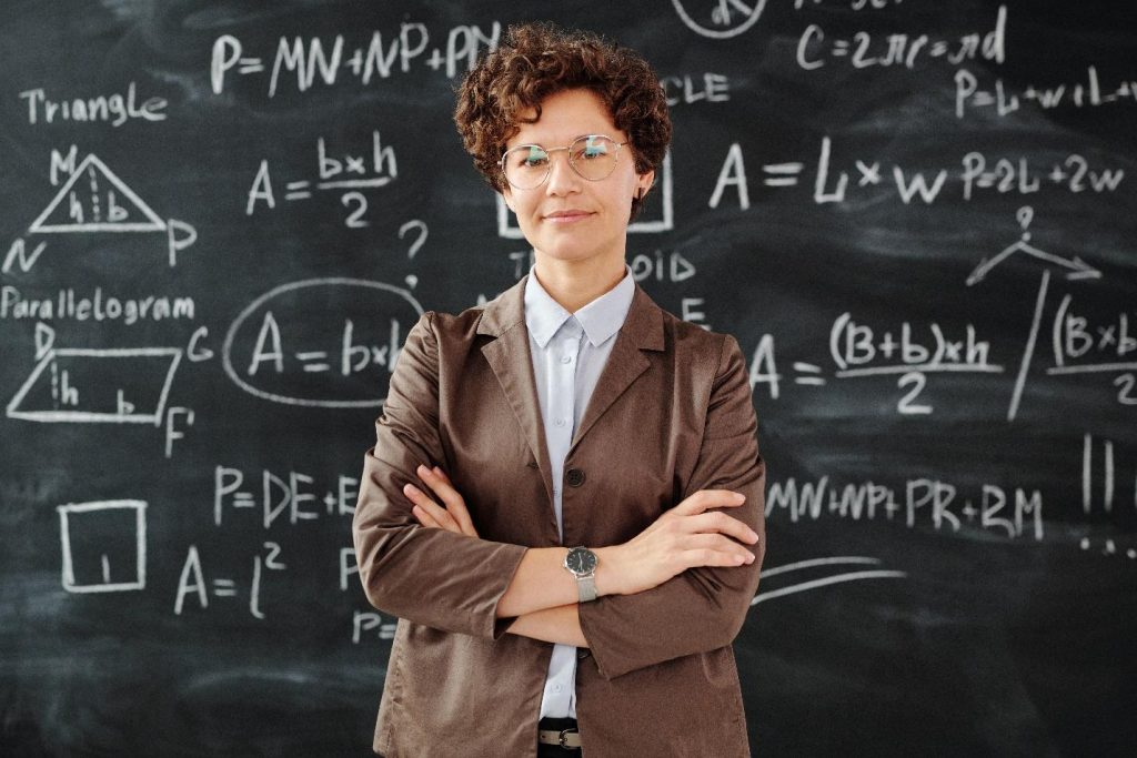 Teacher with arms crossed standing in front of blackboard