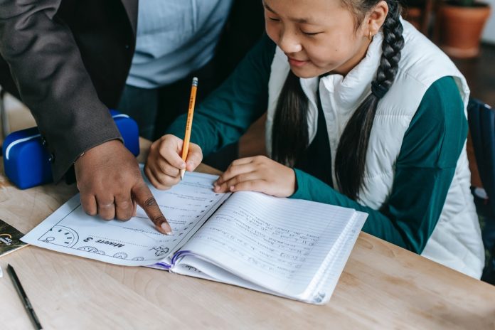 Young girl writing on a worksheet with a teacher helping
