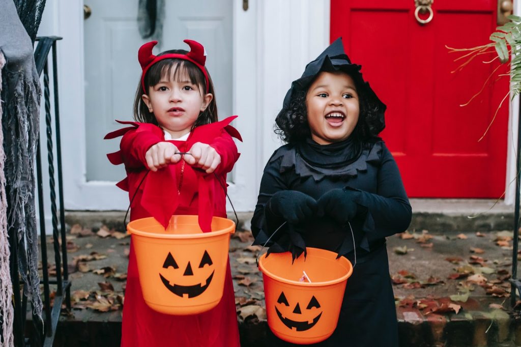 Two young girls in Halloween costumes holding out their trick or treating buckets