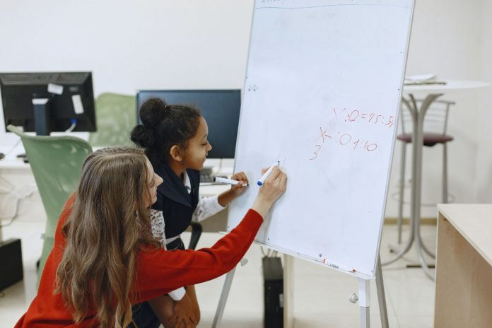 Teacher helping a child with a math problem on a whiteboard