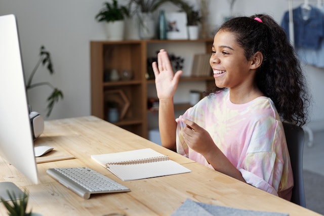 Girl sitting at desk smiling and waving at computer