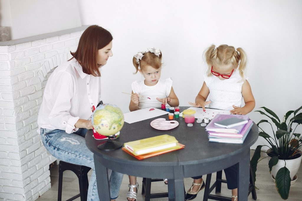Kids painting at a table while their mother watches them