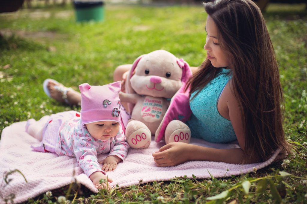 A mother and her baby on a picnic blanket with a large stuffed rabbit