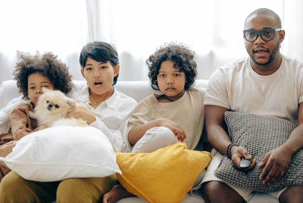 A family of four shares a couch as they watch TV