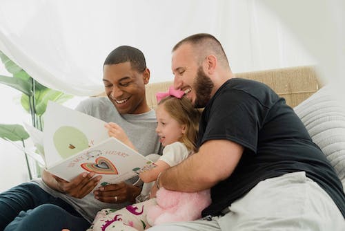 Two men reading book and laughing with daughter