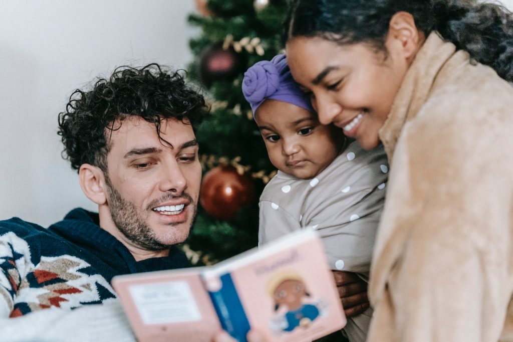 Parents reading a book to baby near Christmas tree