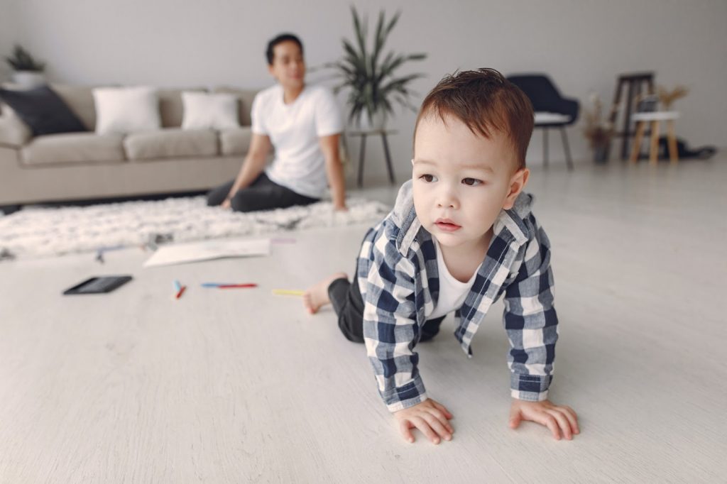 Young boy crawls on the floor with his father watching in the foreground