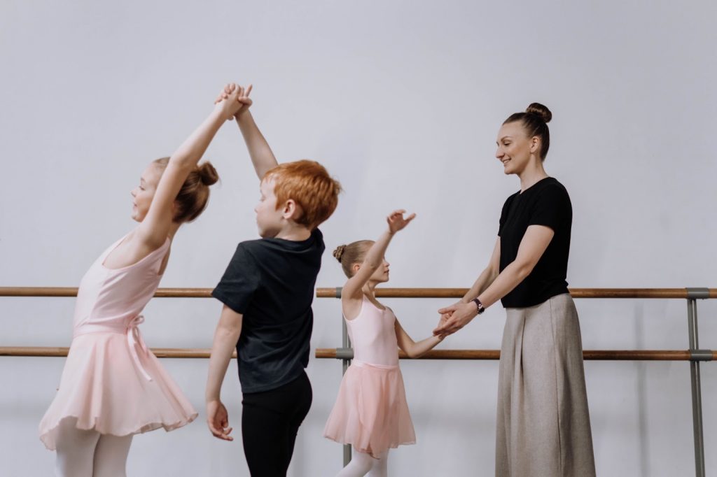 Three children learn ballet with an instructor in the foreground