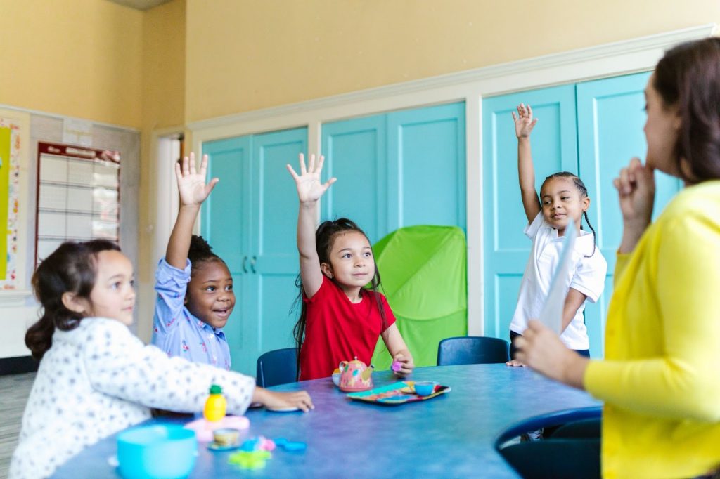 Children sitting around a table with raised hands