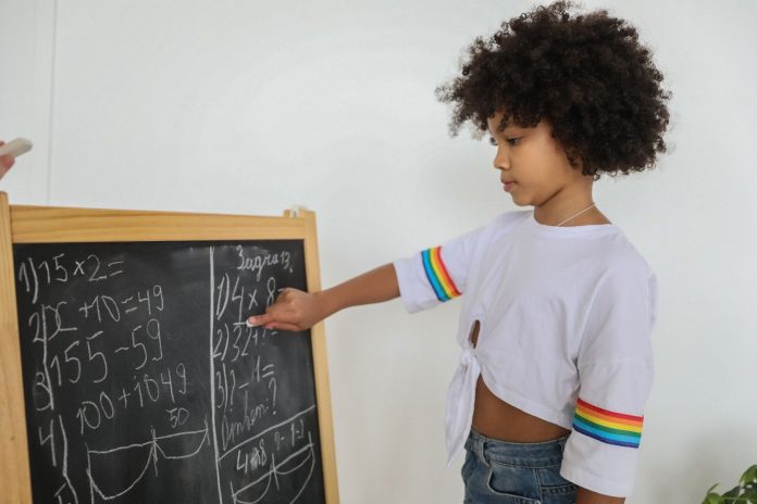 Child solving math problem on a blackboard placed on the floor