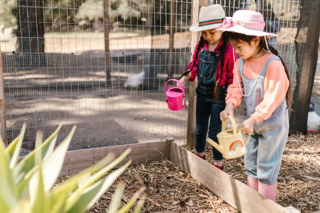 Two young girls using water cans in a garden