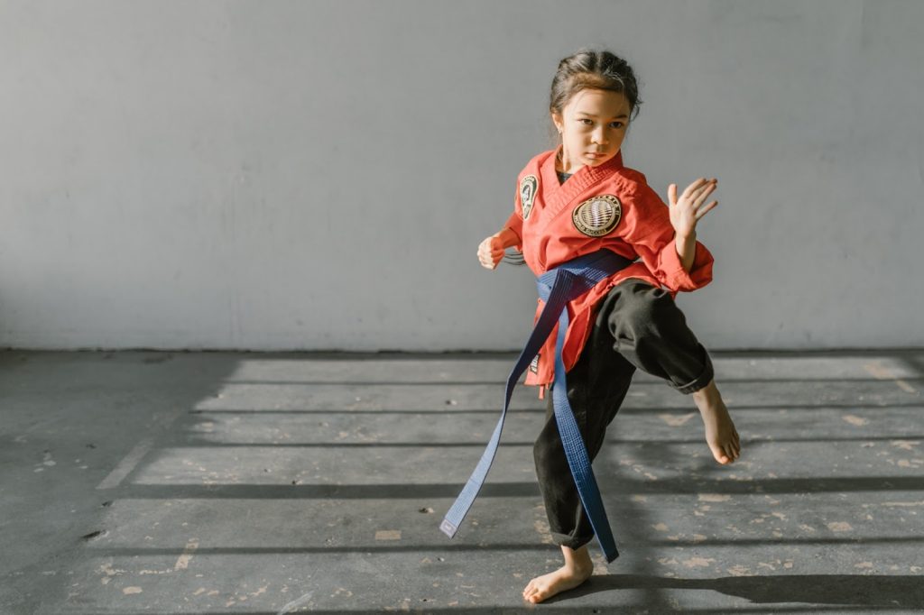A young girl in a red Dobok and blue belt practices tae kwon do