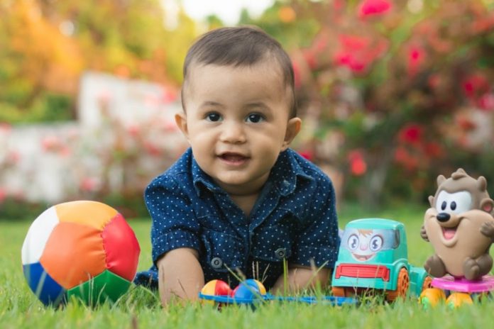 Smiling toddler surrounded with toys plays outdoors