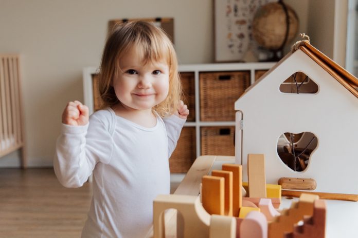 Smiling toddler plays with wooden house