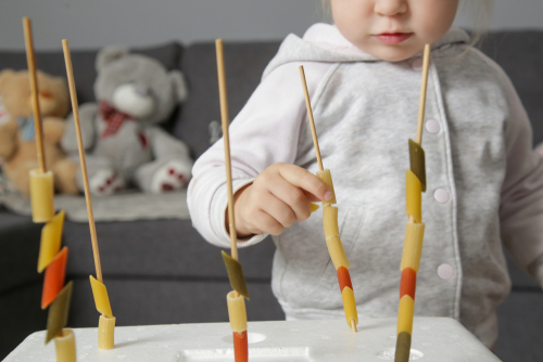 Young girl threading different color rigatoni pastas