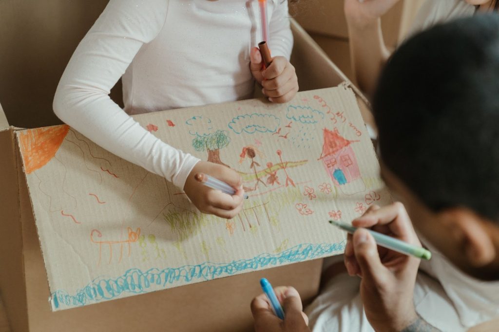 Two kids drawing on cardboard with glitter pens