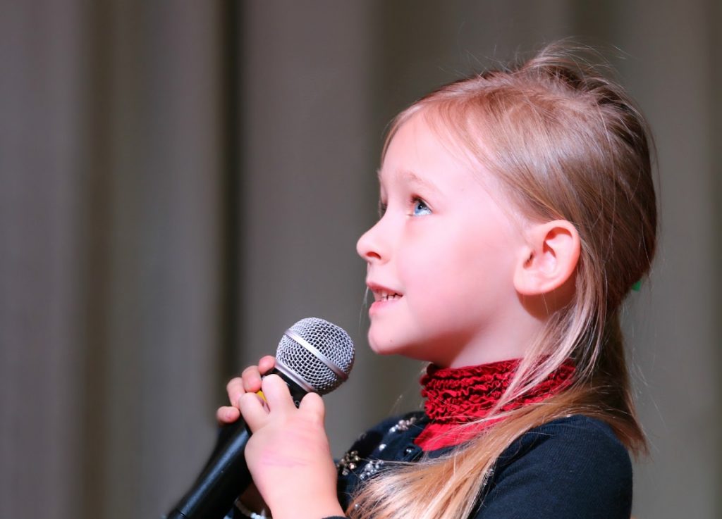 A young girl holds up a microphone as she prepares to sing
