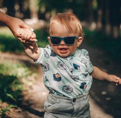 A toddler walking in the park wearing sunglasses