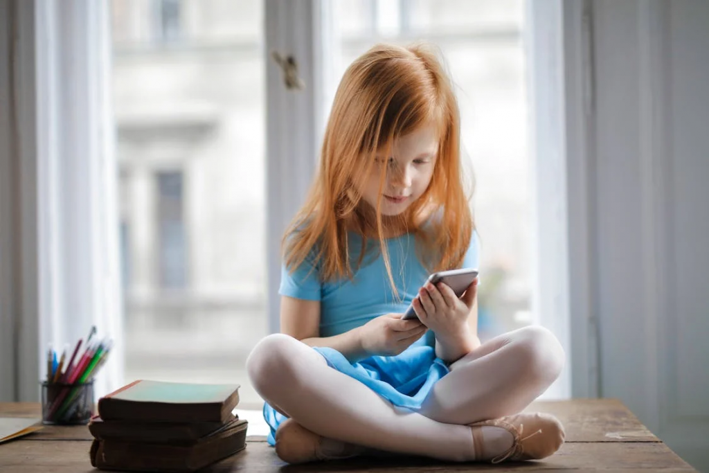 A young girl using a phone sitting on a desk