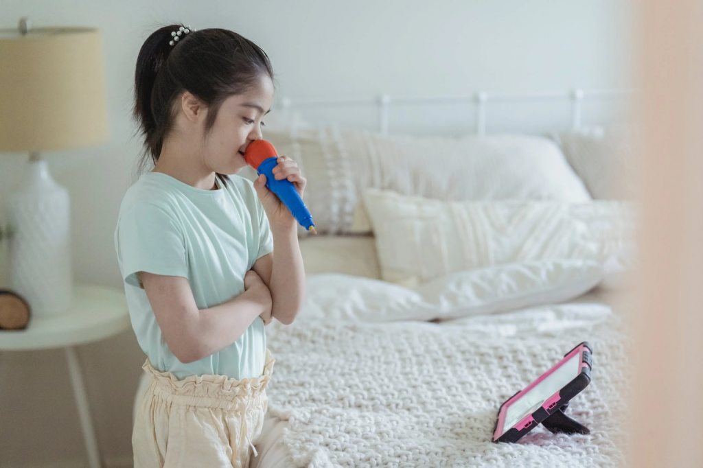 A young girl holds a microphone while looking at a tablet