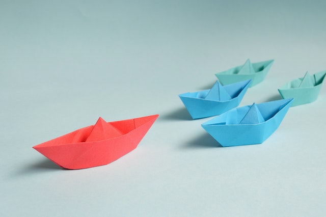 A red paper boat with two blue and two green paper boats