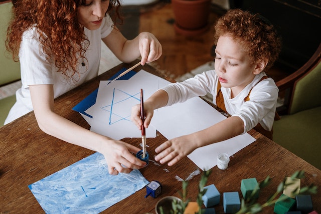 A woman helping a child paint on sheets of paper