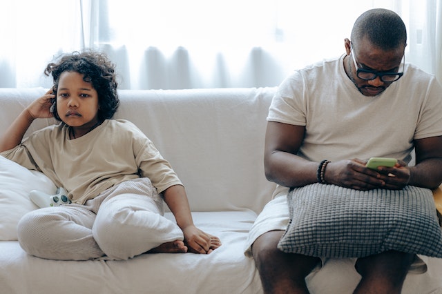 Child sitting on a couch with a parent who is busy on their phone