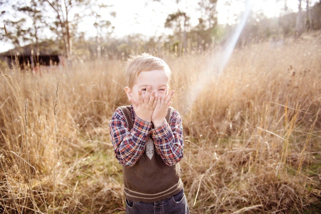 Child in a field covering his face with his hands