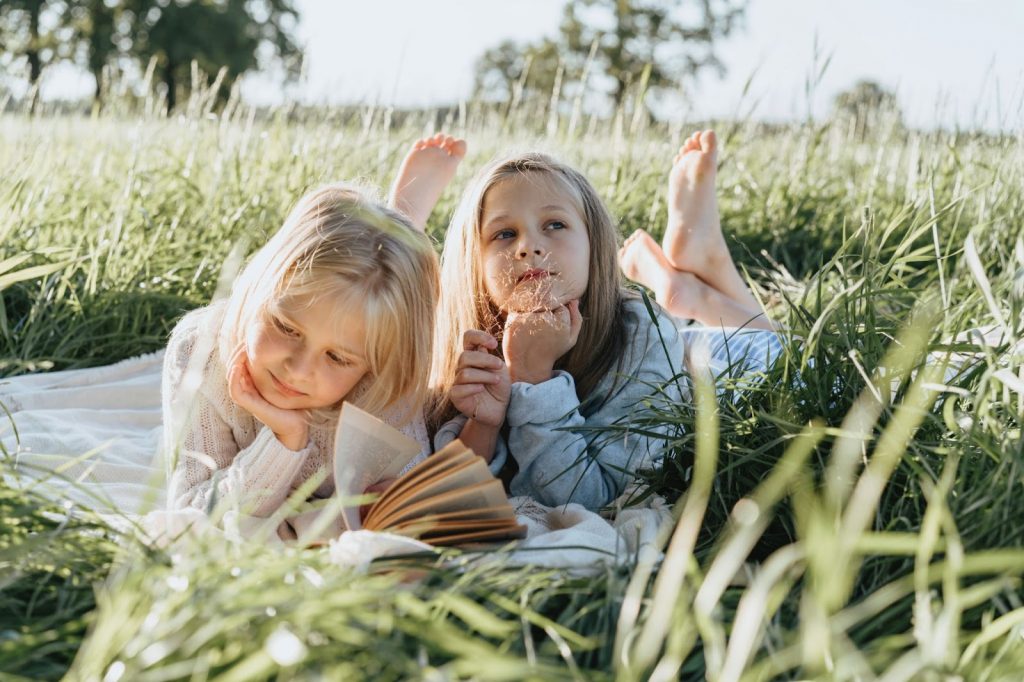 Little Girls Lying on Green Grass Field Reading