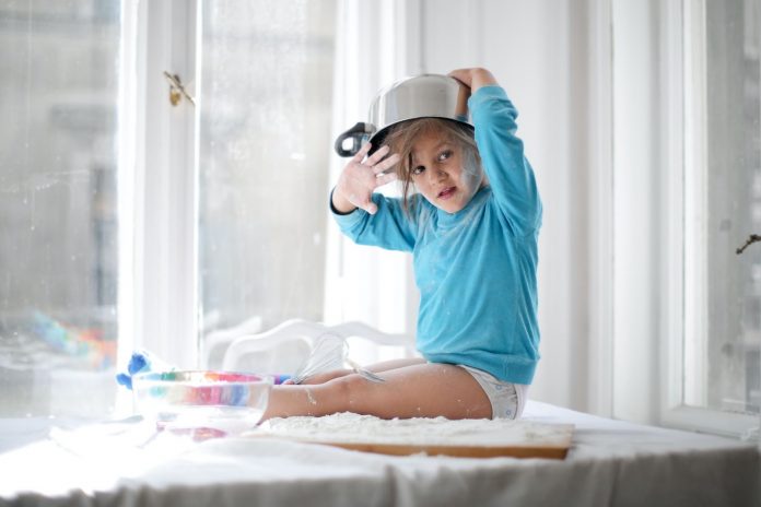 Little girl playing with pan and flour in kitchen