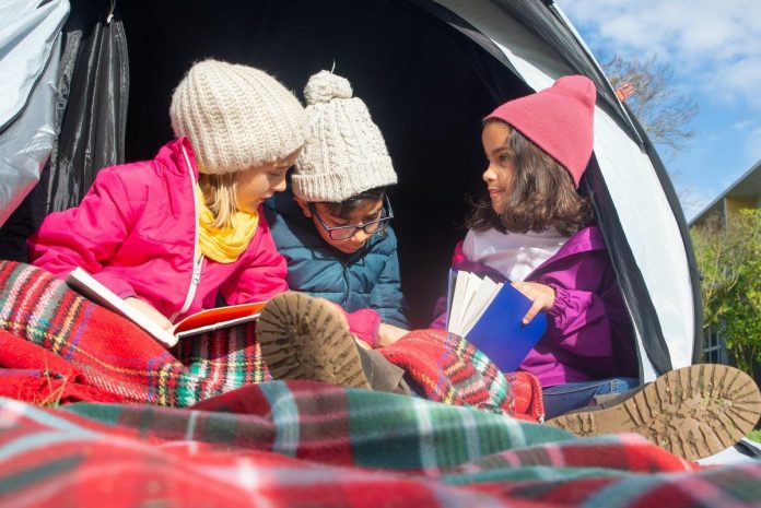 Children reading books under a tent