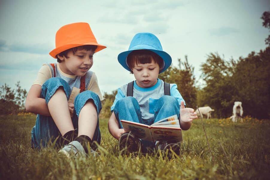 Two children reading in a book in a grass field
