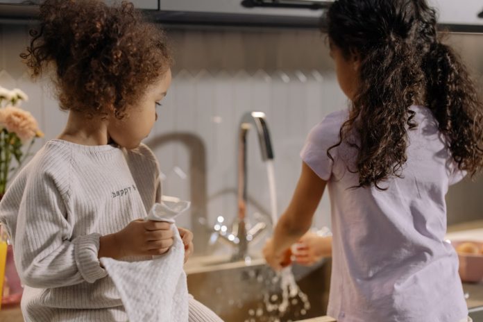 Two young girls wash and dry dishes by a sink