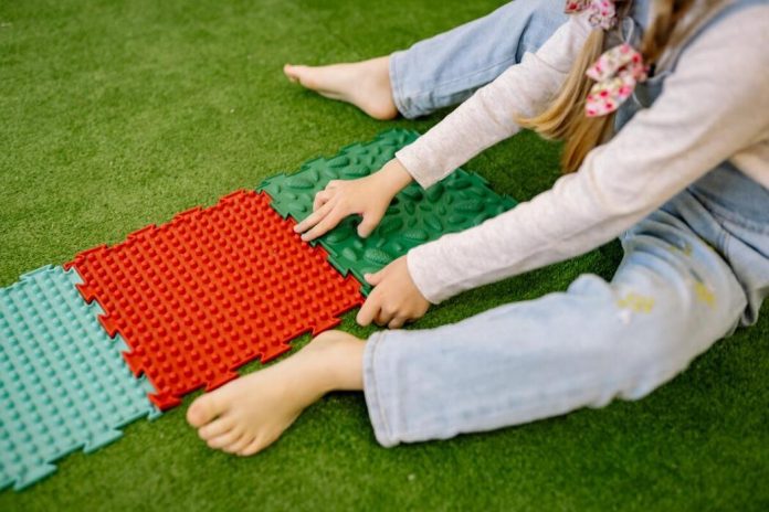 A little girl sitting on the grass and playing with plastic mats