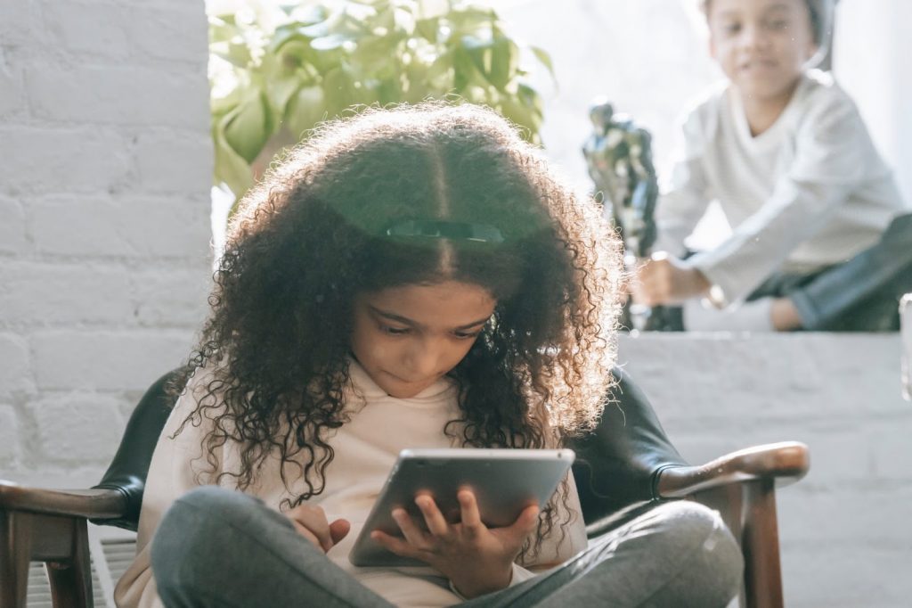 Young girl looks into a tablet while seated on a chair