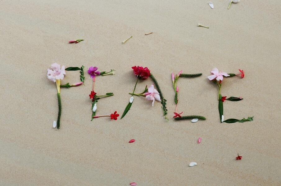 Word Peace written on sand with flowers