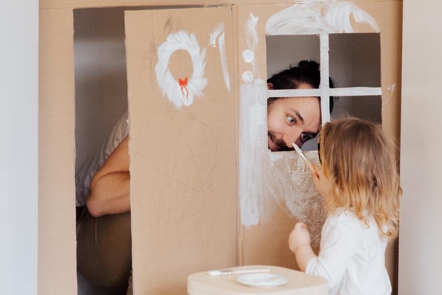 A little girl painting on the cardboard house