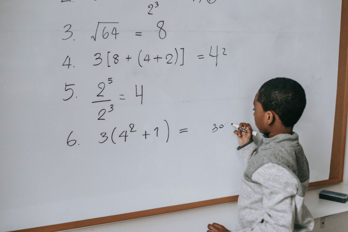 Schoolboy solving math examples on whiteboard