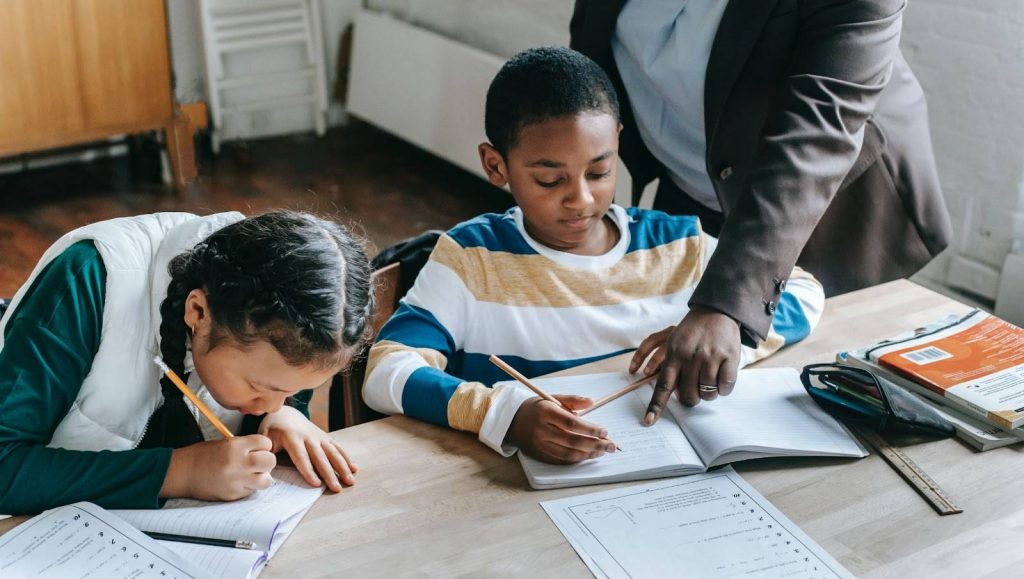 Teacher helping two kids with writing