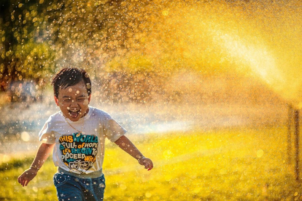 Little boy running in the park under sprinklers