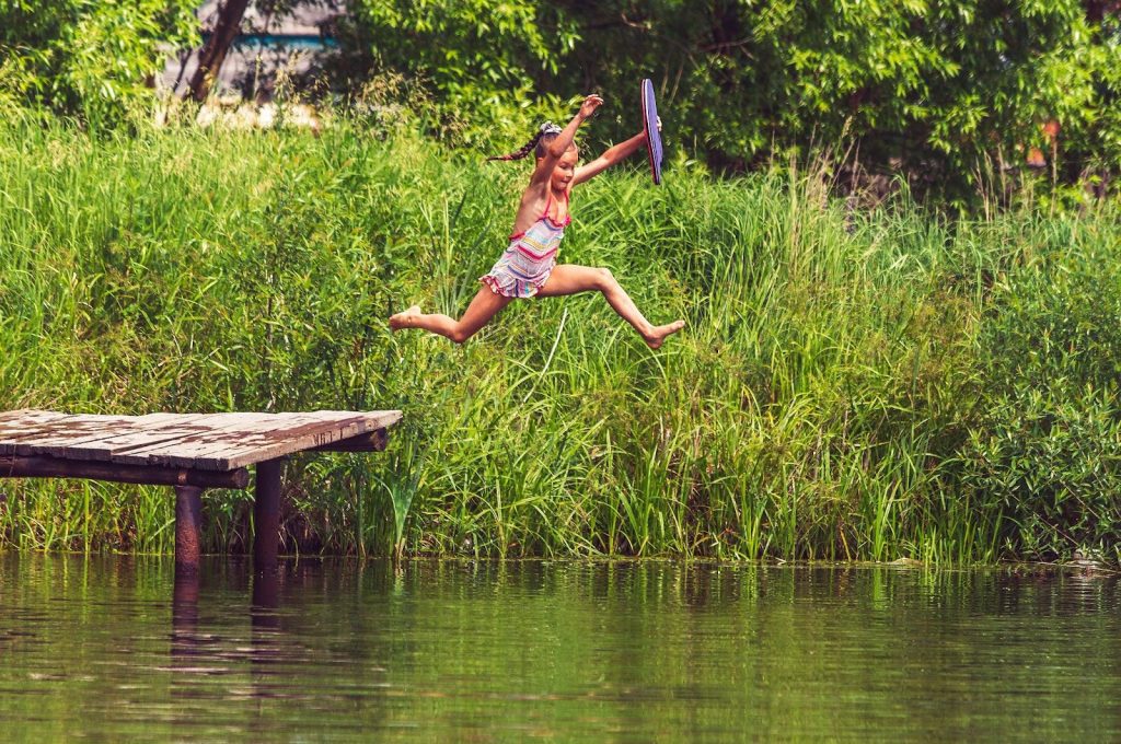 Little girl jumping in a lake from a wooden dock