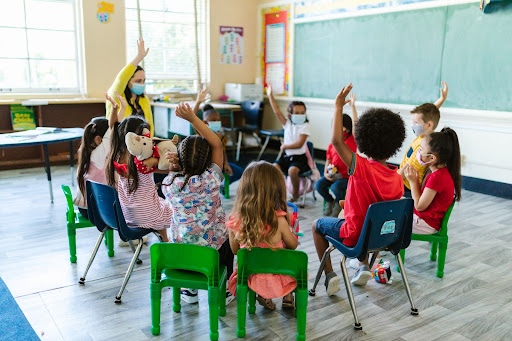 Teacher and kids raising their hands in the classroom