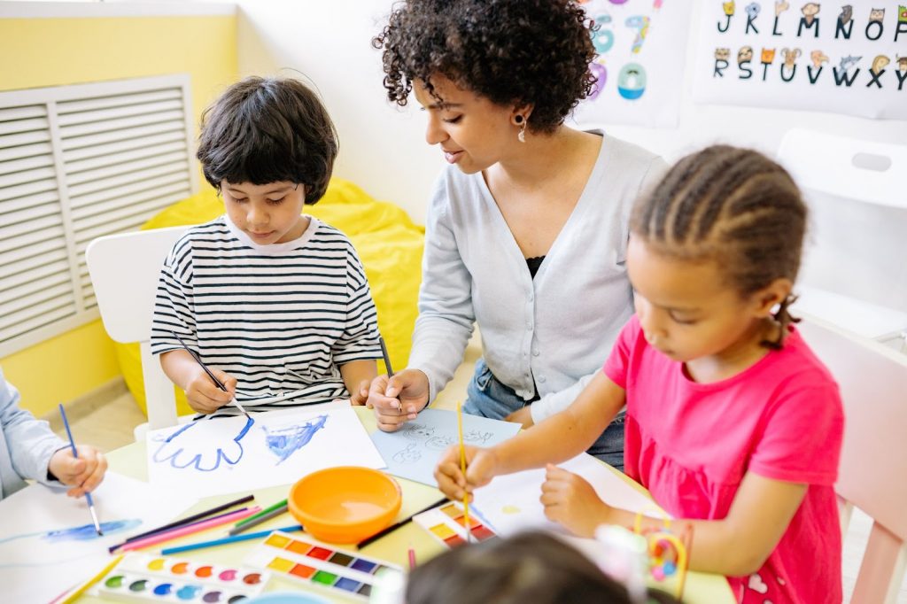 Boy and girls painting with teacher next to them