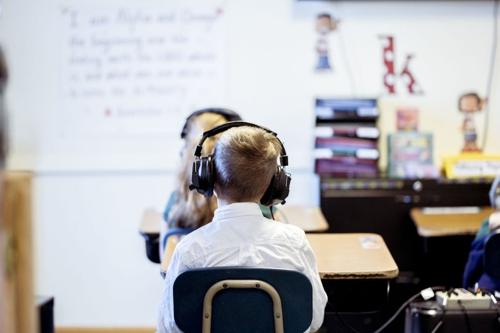 A focus shot of a kid wearing headphones sitting in the classroom