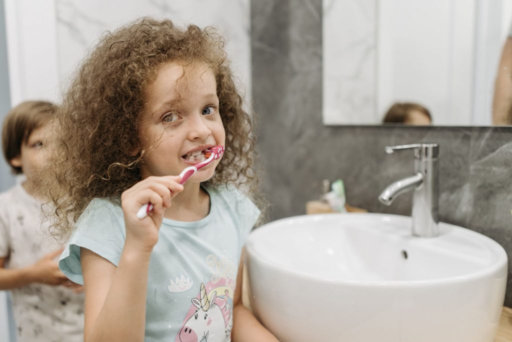 A little girl brushing her teeth with a red toothbrush