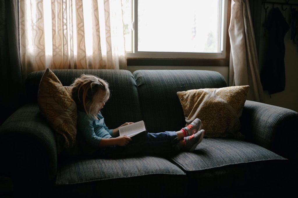 Little girl sitting on a couch and reading a book