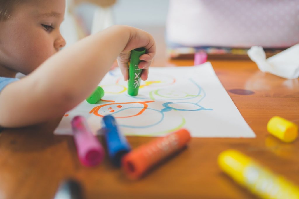 A baby coloring a white sheet of paper with crayons