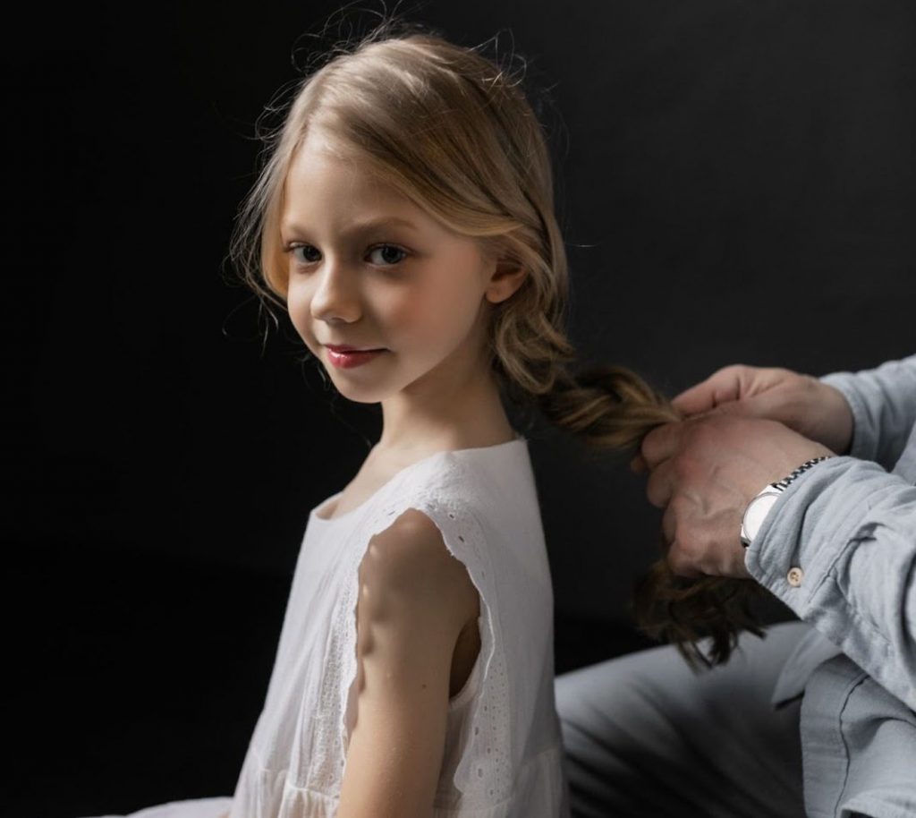 A girl dressed in white getting her hair braided